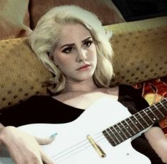 a woman sitting on a couch holding a white guitar