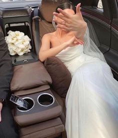 a woman in a wedding dress laying on the back of a car with her hand up to her face