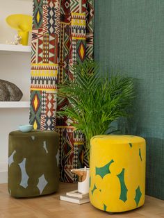 two brightly colored stools sit in front of a green wall with decorative designs on it