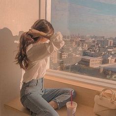 a woman sitting on top of a window sill next to a cup and purse