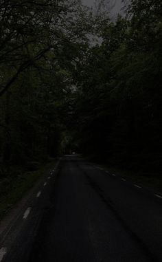 an empty road in the dark with trees on both sides and one light at the end