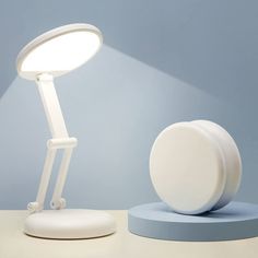 a white desk lamp sitting on top of a table next to a round light fixture