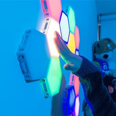 a person holding up a multicolored light in front of a wall mounted device