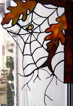 a stained glass window with leaves and spider web on it's side, in front of a house