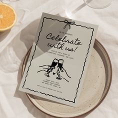 a plate with a card that says celebrate with us and two glasses of wine on it