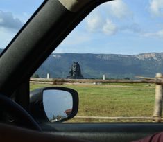 a view from the inside of a car looking out at mountains and grass in the distance