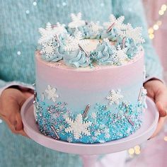 a person holding a cake with frosting and decorations on the top, in front of a christmas tree