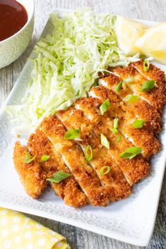 some food is on a white plate and next to a bowl of sauce, lemon wedges, and lettuce