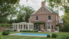 a large brick house with a pool in the front yard, surrounded by hedges and trees