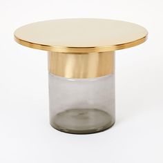 a small round table with a gold top and glass vase on the bottom, sitting in front of a white background