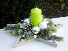 a green candle sitting on top of a wooden star shaped centerpiece with pine cones and ornaments