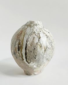 a white and gray vase sitting on top of a table next to a white wall