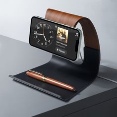 an alarm clock with a pen on top of it and a cell phone in the holder