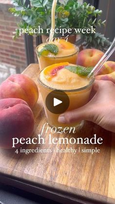 a person holding a glass with peach lemonade in it on top of a wooden cutting board