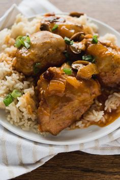 a white plate topped with rice and meat covered in sauce on top of a wooden table