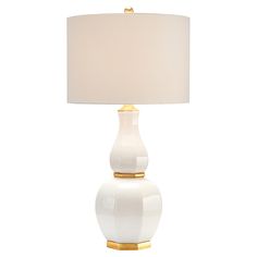 a white lamp with a gold base on a white table cloth shade is shown in front of a white background