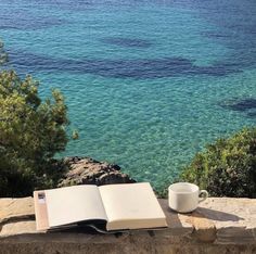 an open book sitting on top of a stone wall next to the ocean