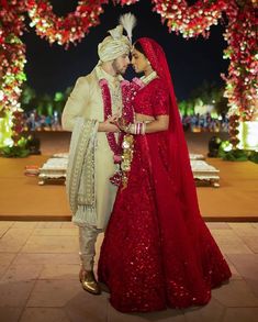 two people dressed in red and white standing next to each other under an archway decorated with flowers