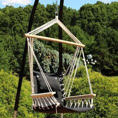 a chair hanging from a metal pole in the middle of a field with trees and bushes behind it