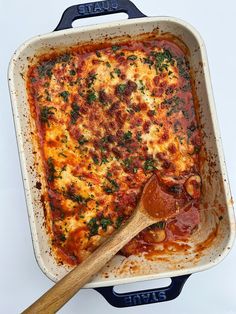 a casserole dish with meat, cheese and sauce in it next to a wooden spoon