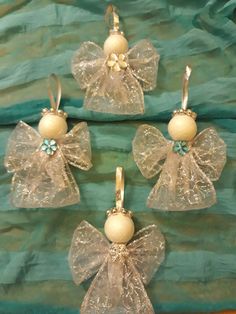 four glass angel ornaments with bows and pearls hanging from the sides on a green cloth