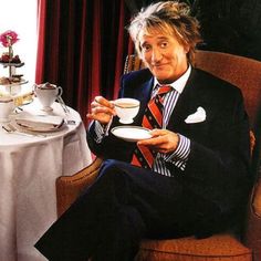 a man sitting in a chair holding a cup and saucer