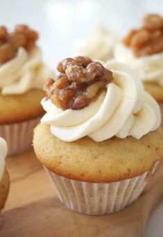 cupcakes with white frosting and walnut toppings on a wooden cutting board