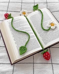 an open book with crocheted flowers on it and a strawberry attached to the page