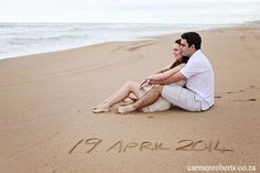 a man and woman are sitting on the beach with their name written in the sand