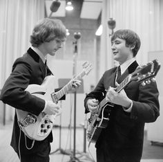 two young men are playing guitars in a recording studio, one is wearing a suit and the other has a tie