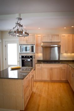 an empty kitchen with wooden floors and stainless steel appliances on the counter top, along with a chandelier hanging from the ceiling