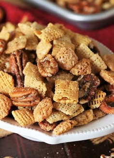 a white bowl filled with chex mix on top of a wooden table next to other snacks