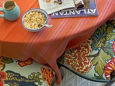 a bowl of cereal sits on an orange tablecloth next to a blue teapot