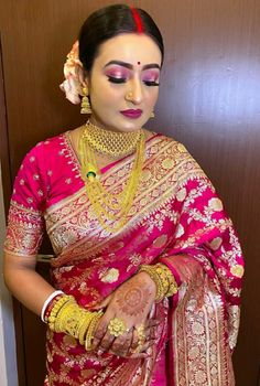 a woman in a pink sari with gold jewelry on her head and hands clasped together