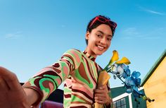 a woman holding a banana and flowers in front of a yellow building on a sunny day