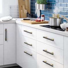 a kitchen with white cabinets and blue tile backsplash, pots on the stove