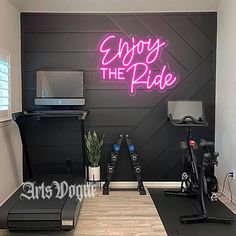 a gym room with exercise equipment and neon sign that says enjoy the ride on the wall