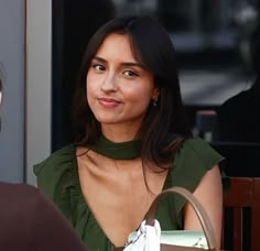 a woman sitting at a table in front of a window with her hand on the purse