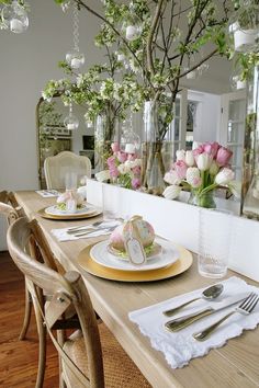 a dining room table set for two with plates and flowers in vases on it