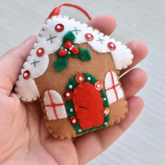 a hand holding a small felt ornament with a gingerbread house on it