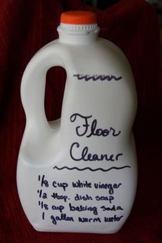 a white jug with writing on it sitting on top of a red cloth next to a bottle