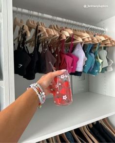 a person is holding a cup in front of a rack with bras on it