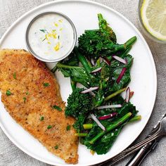 a white plate topped with fish and veggies next to a bowl of ranch dressing