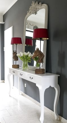 a white table topped with a vase filled with flowers next to a mirror and lamp