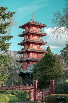 a tall red building sitting on top of a lush green field next to trees and bushes