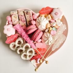 a heart shaped plate filled with lots of different types of candies and cookies on top of each other