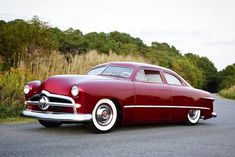 an old car is parked on the side of the road in front of some trees