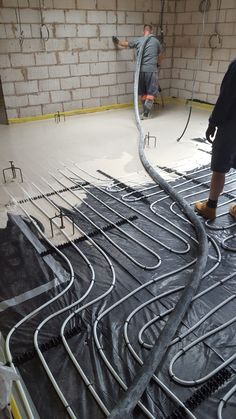 two men are working on the floor in an unfinished room with exposed piping lines