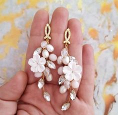 a pair of white flower and crystal earrings in the palm of someone's hand