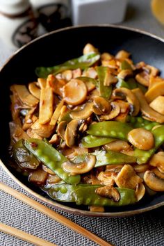 stir fry with mushrooms and green beans in a black bowl next to chopsticks